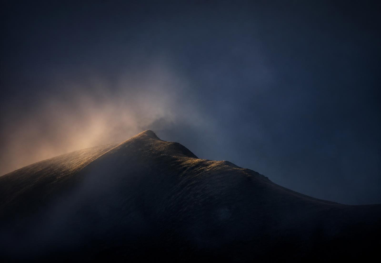 Sunlit mountain summit ridge emerging through morning mist